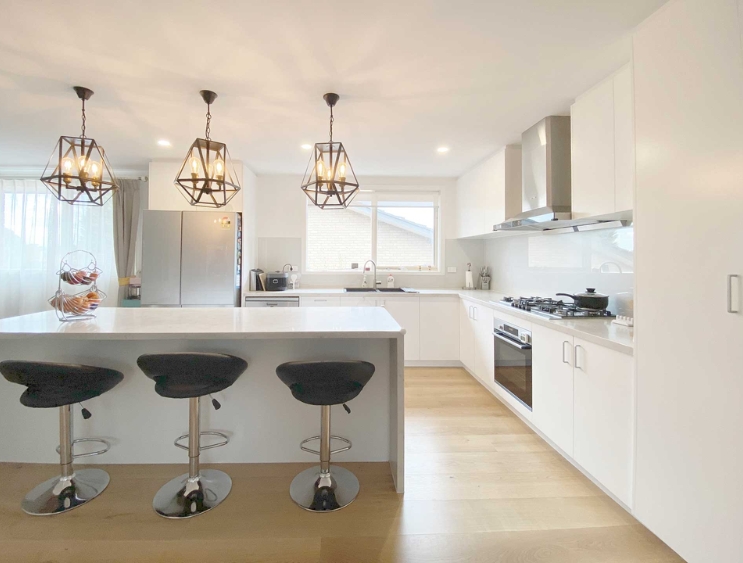 Modern white kitchen with a large island, three stools, pendant lights, and stainless steel appliances. Modern white kitchen with a large island, three stools, pendant lights, and stainless steel appliances.