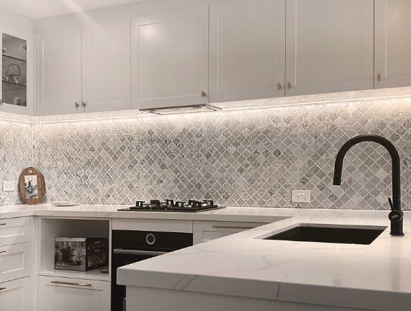 Modern kitchen with white cabinets, marble backsplash, black faucet, and built-in stovetop. Modern kitchen with white cabinets, marble backsplash, black faucet, and built-in stovetop.