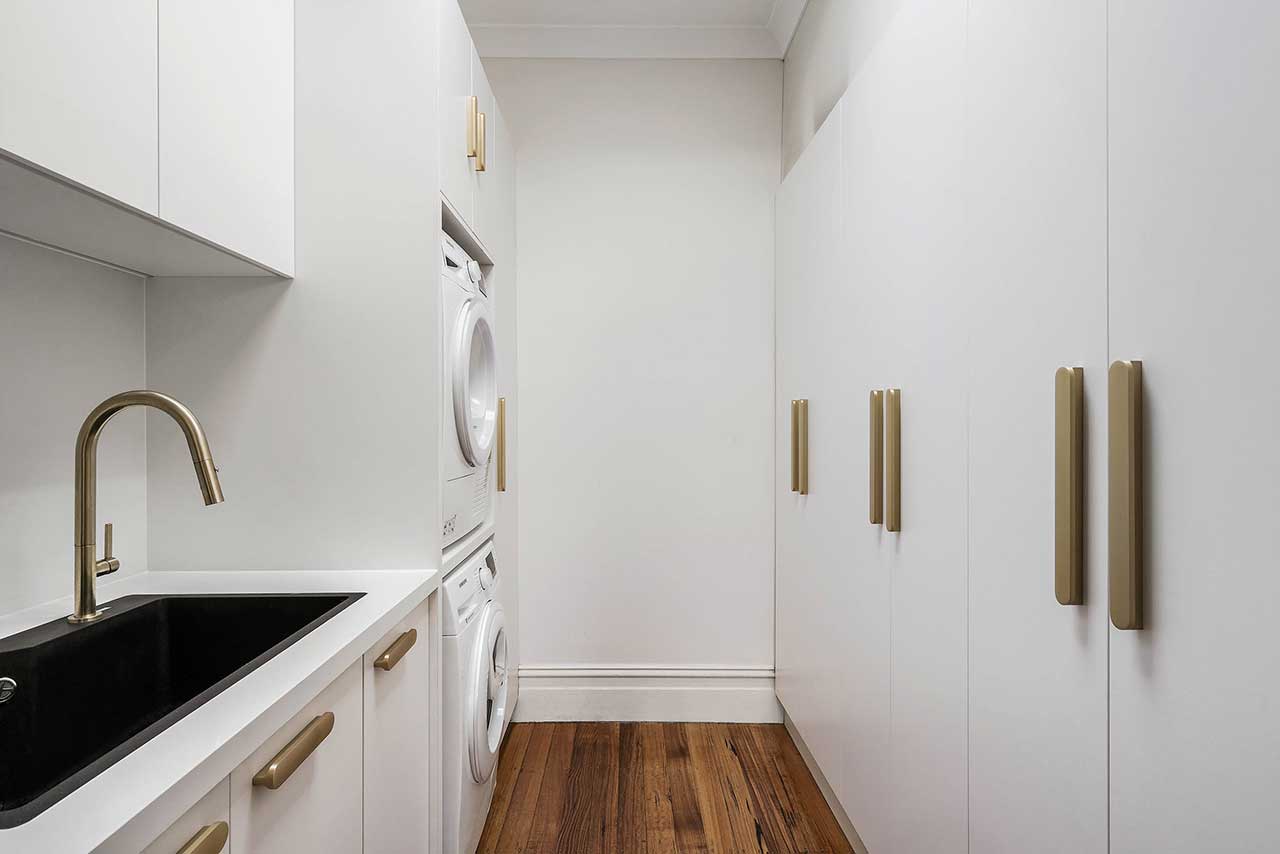 Minimalist laundry room with stacked washer and dryer, white cabinets, gold handles, and a black sink. Minimalist laundry room with stacked washer and dryer, white cabinets, gold handles, and a black sink.