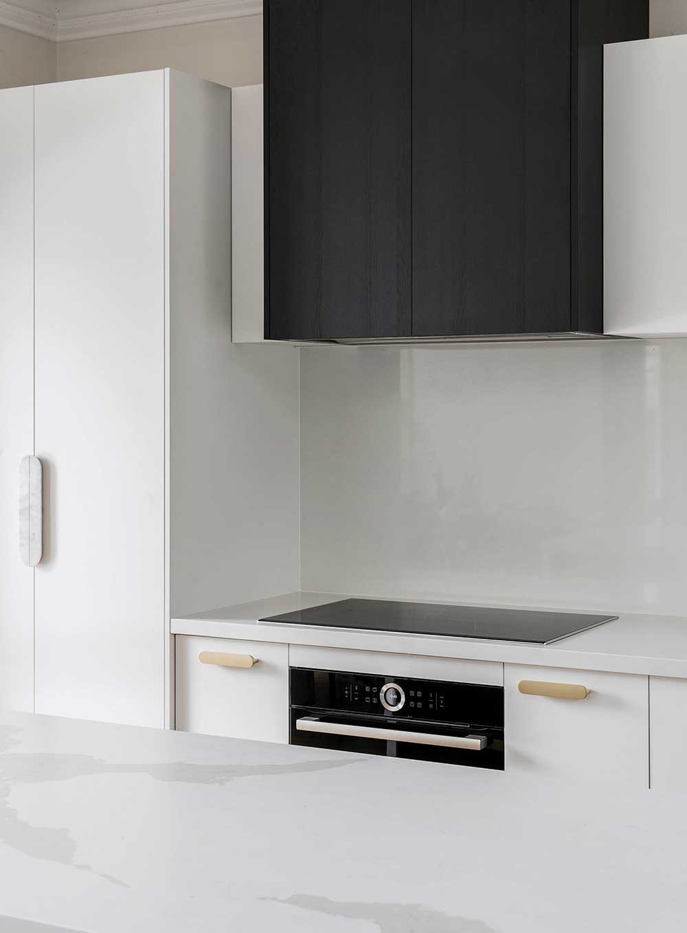 Minimalist kitchen with white cabinets, black hood, and a sleek stovetop on a white countertop. Minimalist kitchen with white cabinets, black hood, and a sleek stovetop on a white countertop.