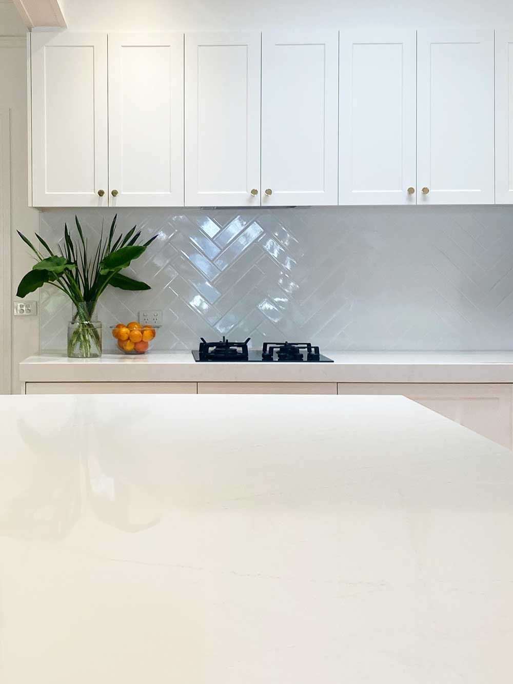 Minimalist kitchen with white cabinets, herringbone tile backsplash, vase of greenery, and a bowl of oranges. Minimalist kitchen with white cabinets, herringbone tile backsplash, vase of greenery, and a bowl of oranges.