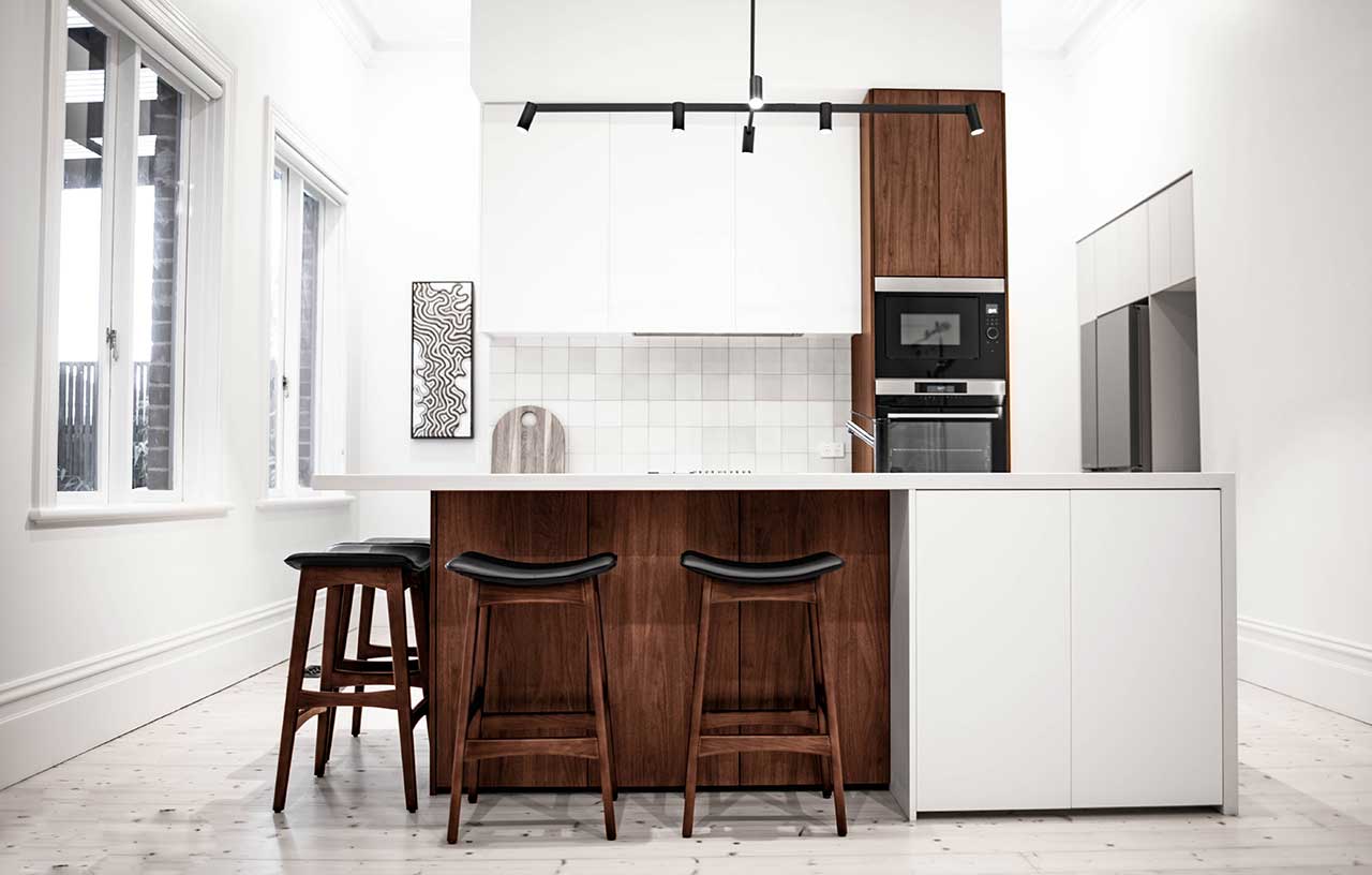 Modern kitchen with a white island, wood accents, three barstools, and built-in appliances under track lighting. Modern kitchen with a white island, wood accents, three barstools, and built-in appliances under track lighting.