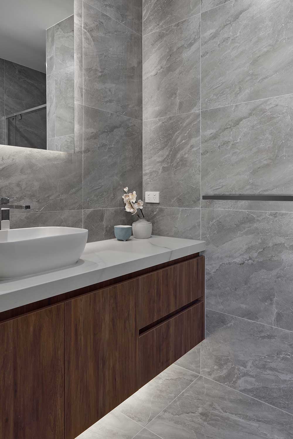 Modern bathroom with gray marble walls, a wooden vanity, white countertop, vessel sink, and small decorative jars. Modern bathroom with gray marble walls, a wooden vanity, white countertop, vessel sink, and small decorative jars.