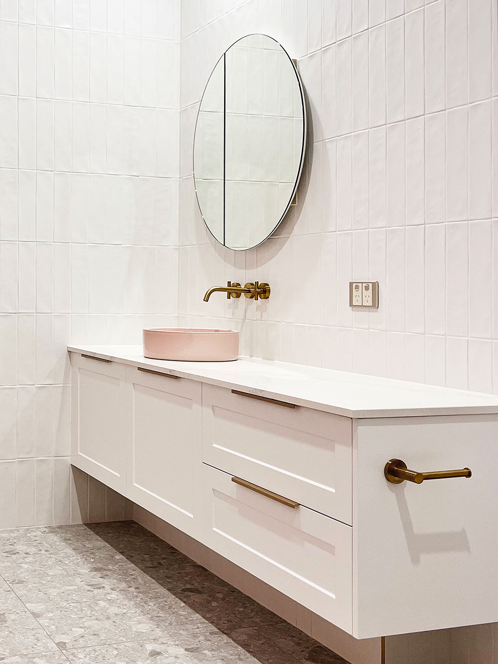 Minimalist bathroom with a white vanity, round mirror, and gold fixtures; features a pink basin and tiled walls. Minimalist bathroom with a white vanity, round mirror, and gold fixtures; features a pink basin and tiled walls.