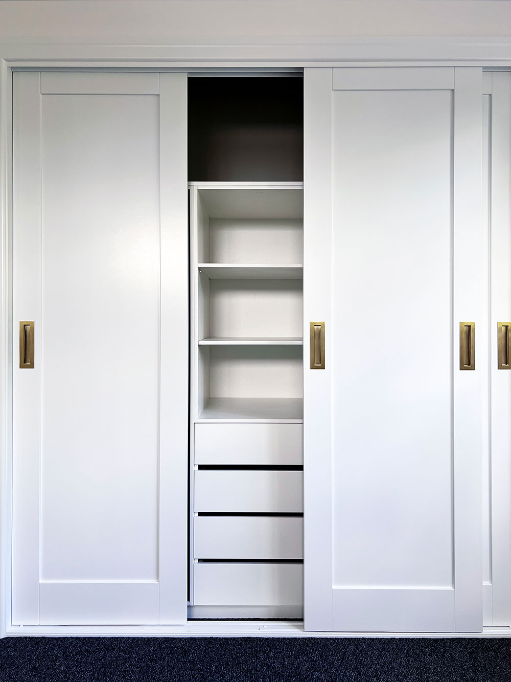 White sliding closet doors partially open, revealing shelves and drawers inside, with brass handles. White sliding closet doors partially open, revealing shelves and drawers inside, with brass handles.
