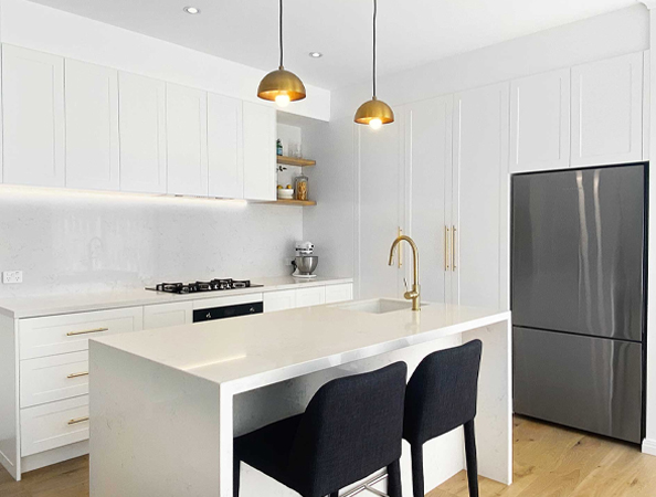 Modern kitchen with white cabinetry, island with stools, gold fixtures, hanging lights, and stainless steel fridge. Modern kitchen with white cabinetry, island with stools, gold fixtures, hanging lights, and stainless steel fridge.