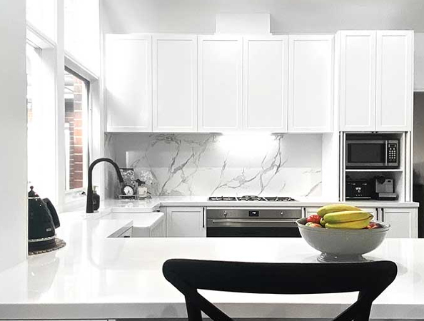 Modern kitchen with white cabinets, marble backsplash, and black fixtures. Bowl of fruit on a sleek countertop. Modern kitchen with white cabinets, marble backsplash, and black fixtures. Bowl of fruit on a sleek countertop.