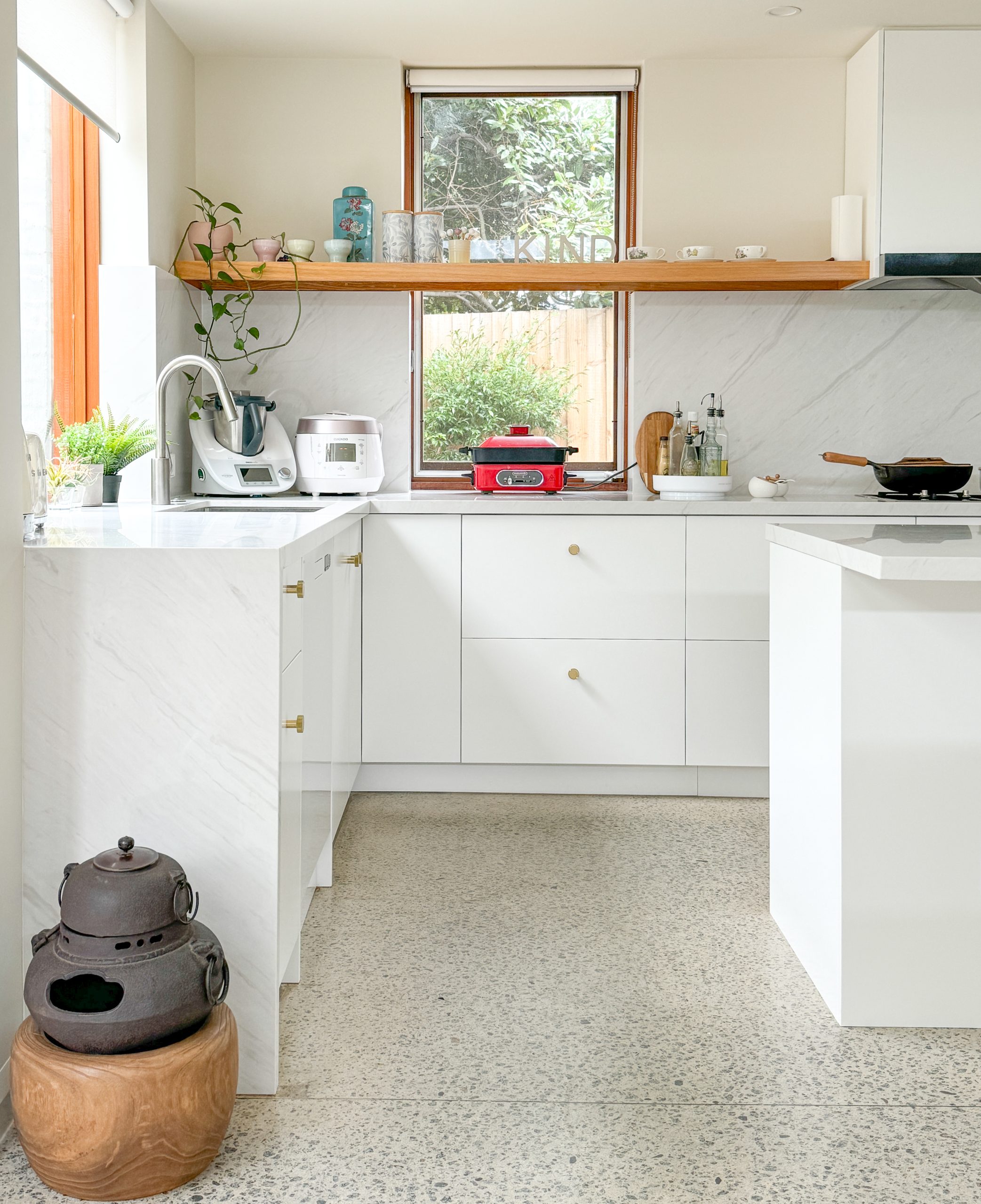 Bright kitchen with white cabinets, countertop appliances, a window, and plants on shelves. Bright kitchen with white cabinets, countertop appliances, a window, and plants on shelves.