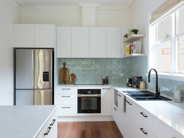 Modern kitchen with white cabinets, stainless steel appliances, light blue tile backsplash, and wooden floor.