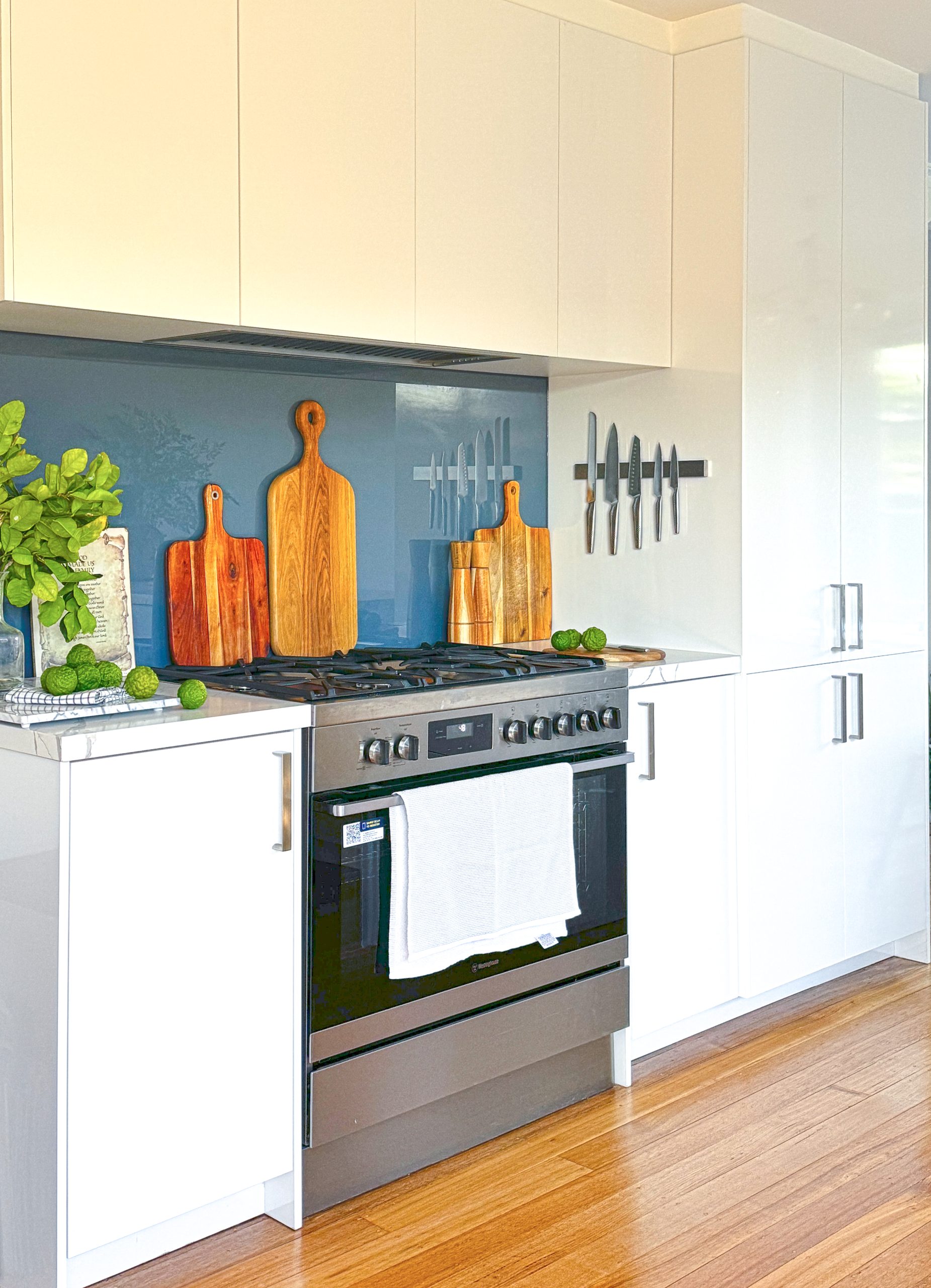 Modern kitchen with a stove, white cabinets, cutting boards, knives on the wall, and limes on the counter. Modern kitchen with a stove, white cabinets, cutting boards, knives on the wall, and limes on the counter.
