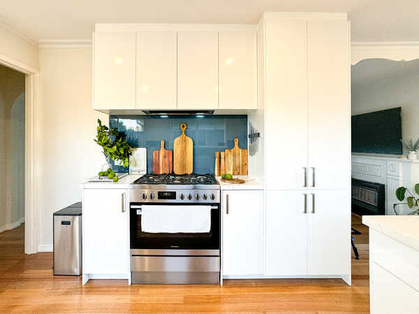 Modern kitchen with white cabinets, stainless steel oven, and cutting boards on countertop.