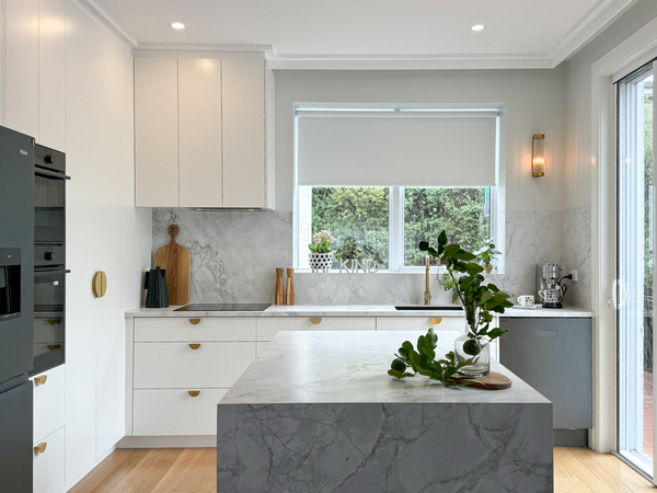 Modern kitchen with white cabinets, marble countertops, and a center island. Large window brings in natural light.