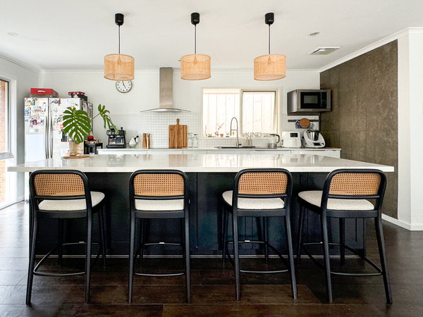 Modern kitchen with a white island, black bar stools, pendant lights, refrigerator, and wall-mounted appliances.