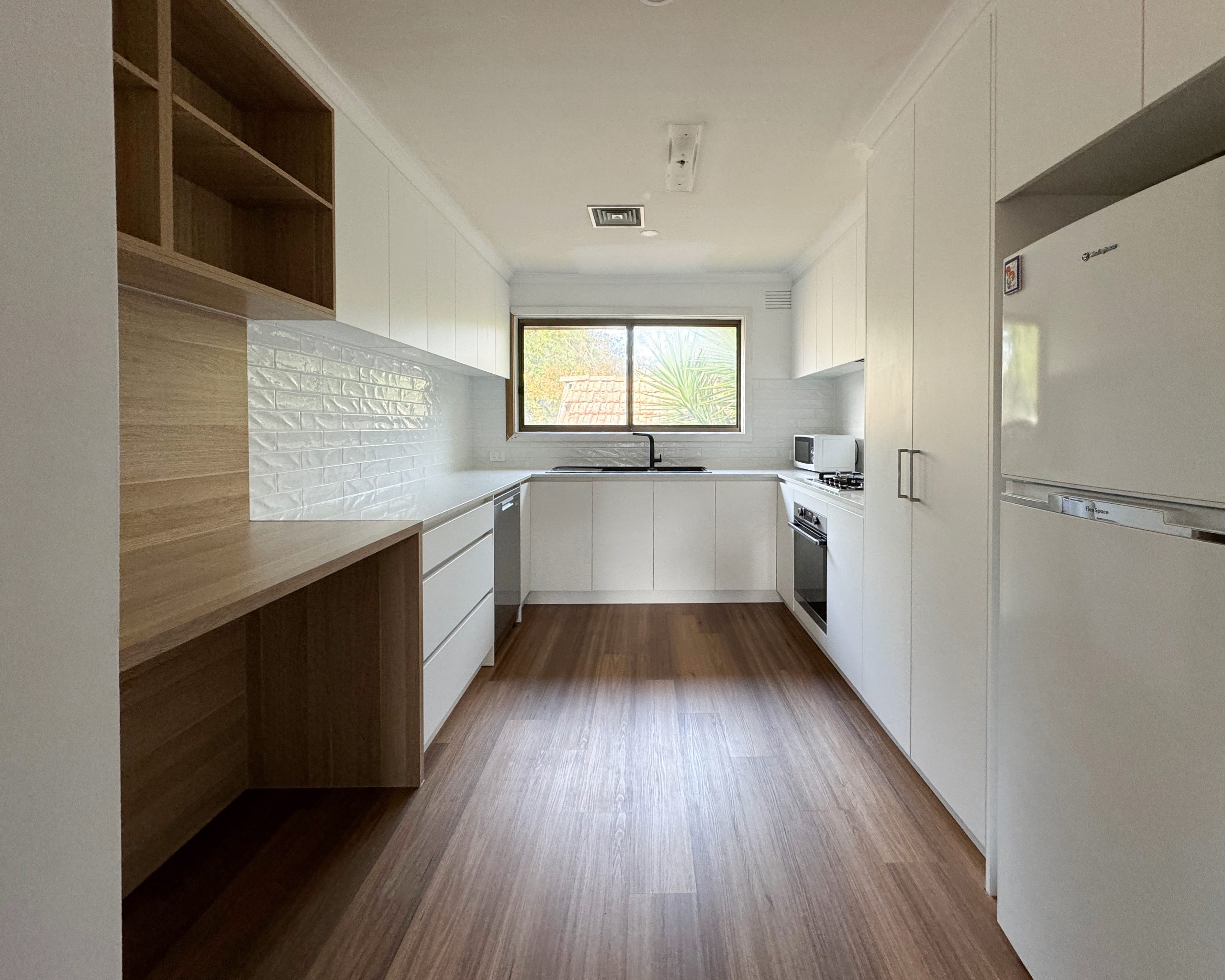 Modern kitchen with wooden floors, white cabinets, wall oven, and a large window providing natural light. Modern kitchen with wooden floors, white cabinets, wall oven, and a large window providing natural light.