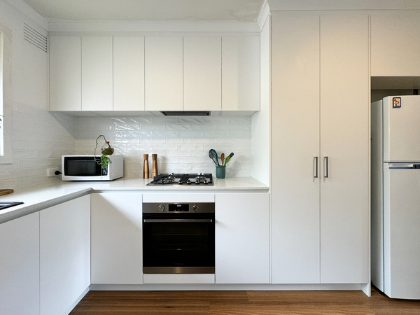 Modern kitchen with white cabinets, built-in oven, stovetop, microwave, potted plant, and a side-by-side refrigerator.