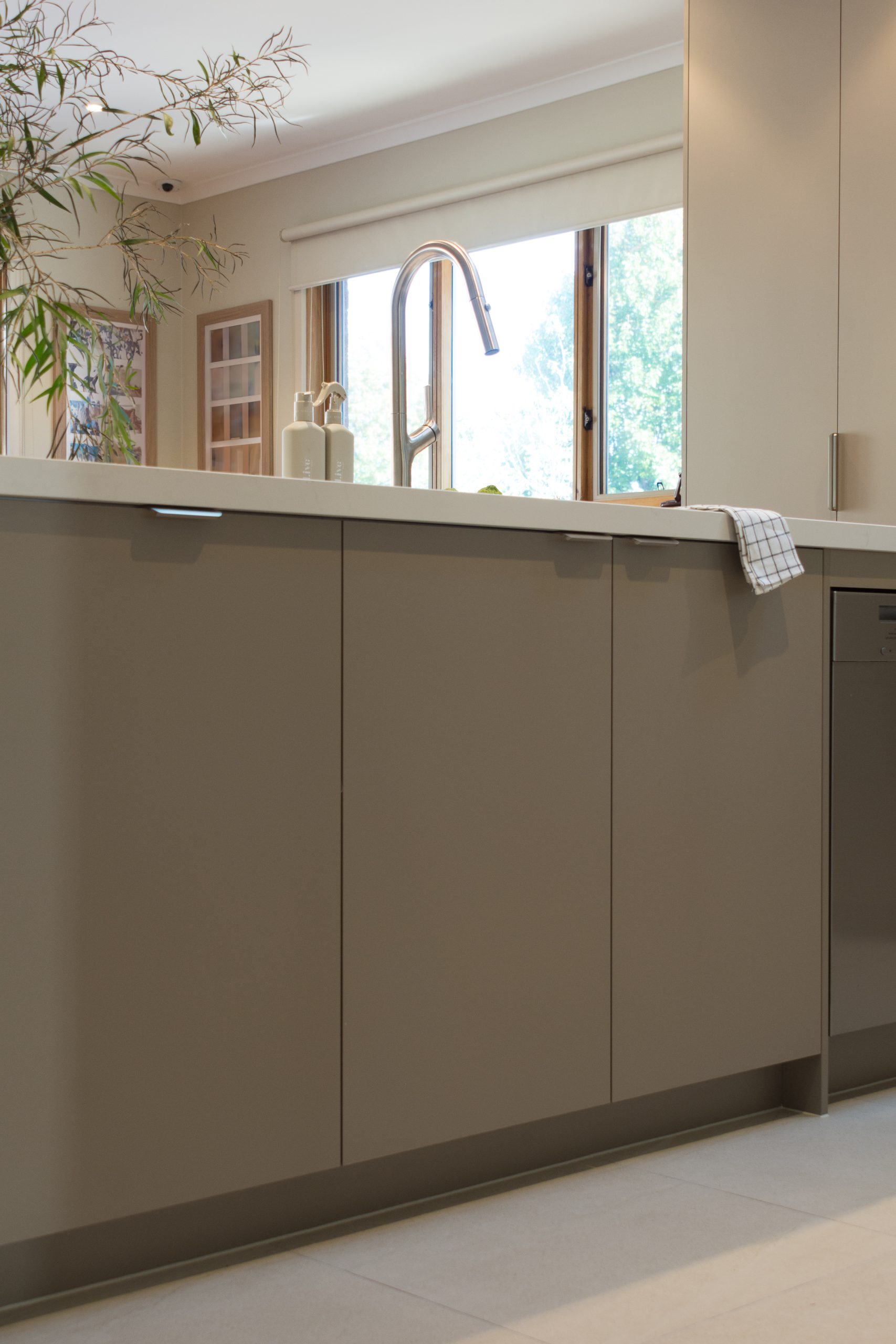 Modern kitchen with beige cabinets, a shiny faucet, and a hand towel. Sunlight streams through large windows. Modern kitchen with beige cabinets, a shiny faucet, and a hand towel. Sunlight streams through large windows.