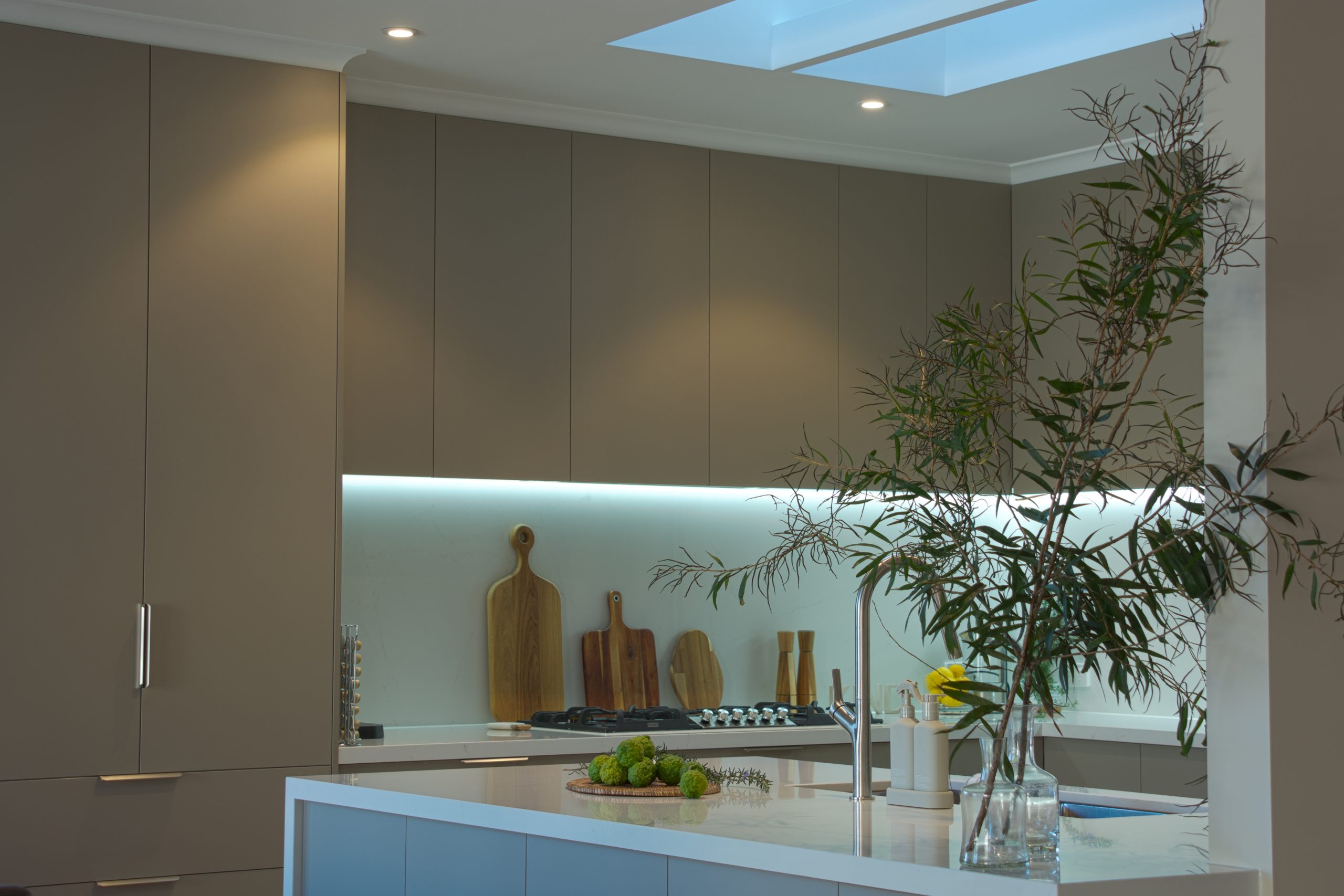 Modern kitchen with sleek cabinetry, chopping boards, a skylight, and a countertop adorned with greenery. Modern kitchen with sleek cabinetry, chopping boards, a skylight, and a countertop adorned with greenery.