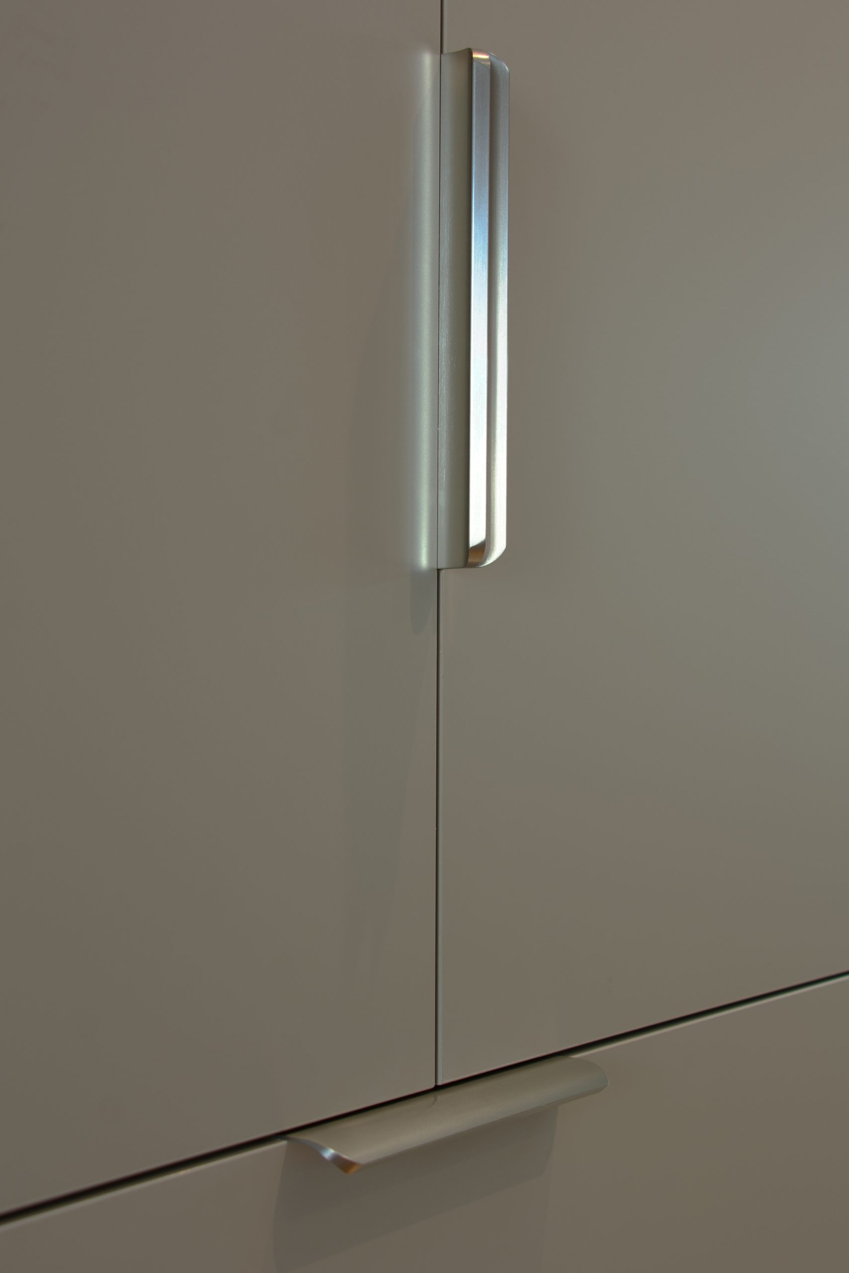 Close-up of a modern, minimalist cabinet with sleek silver handles on a smooth, light-colored surface. Close-up of a modern, minimalist cabinet with sleek silver handles on a smooth, light-colored surface.