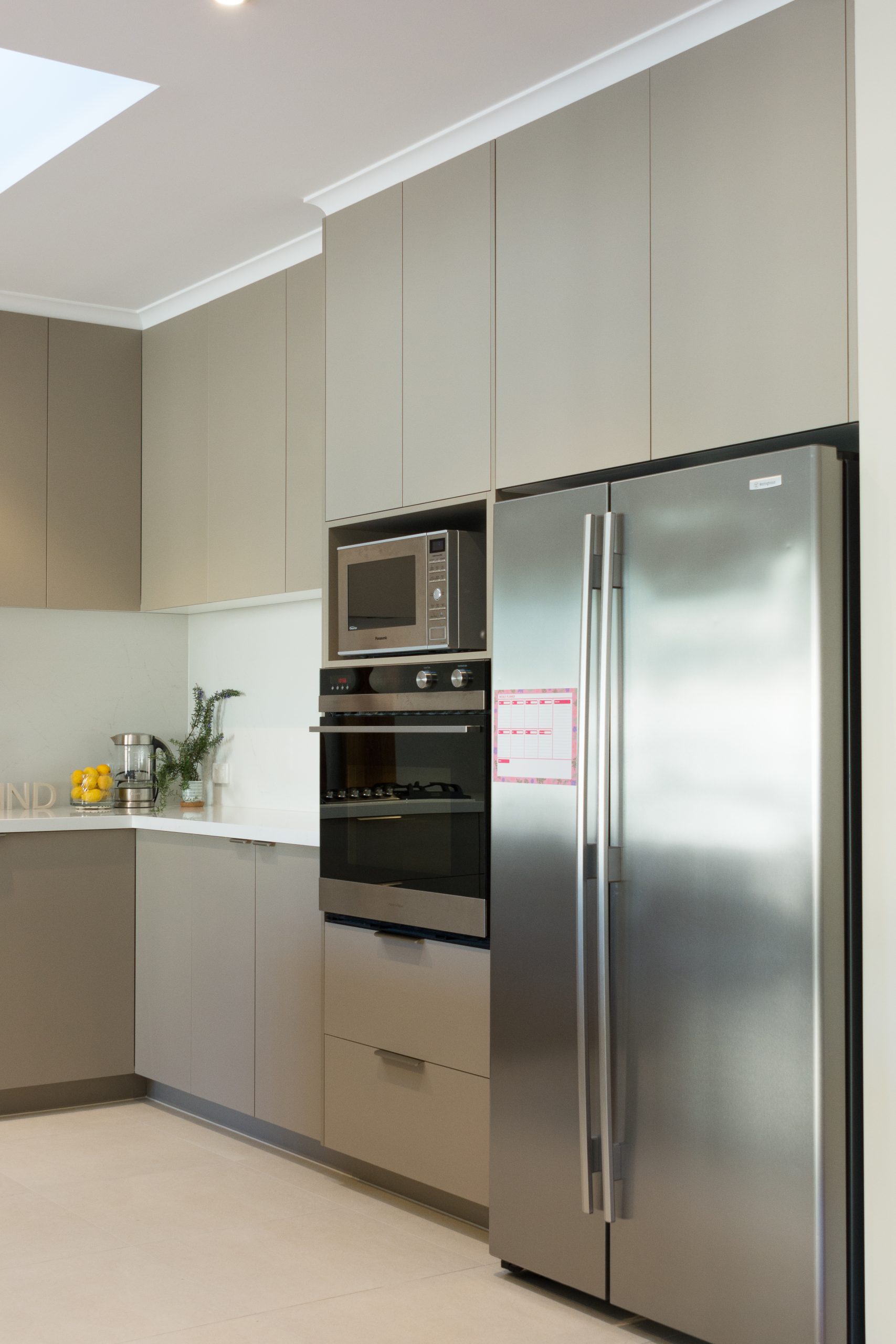 Modern kitchen with grey cabinets, stainless steel fridge, built-in oven, and microwave on cream tile flooring. Modern kitchen with grey cabinets, stainless steel fridge, built-in oven, and microwave on cream tile flooring.