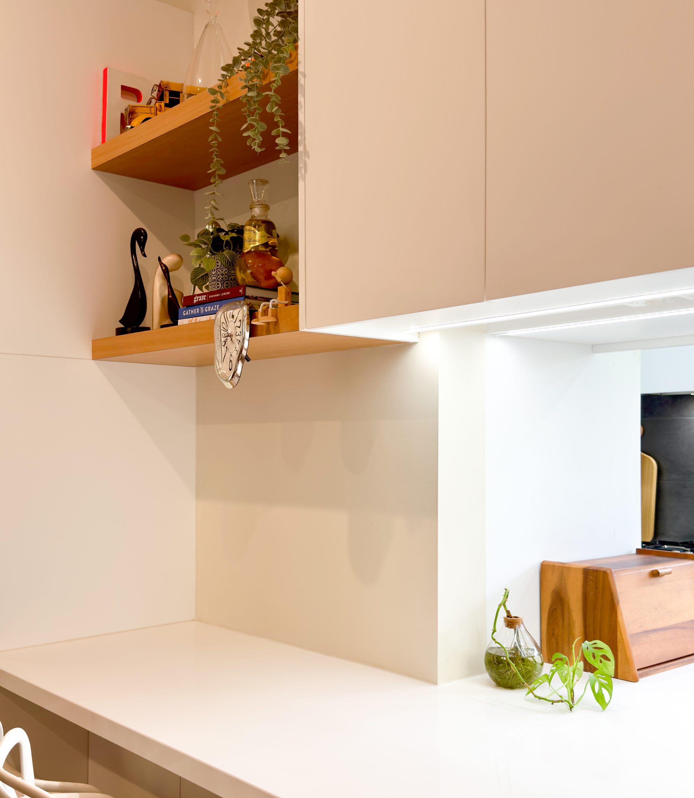 Minimalist kitchen with wooden shelves, plants, books, a clock, and a cutting board on a white counter. Minimalist kitchen with wooden shelves, plants, books, a clock, and a cutting board on a white counter.