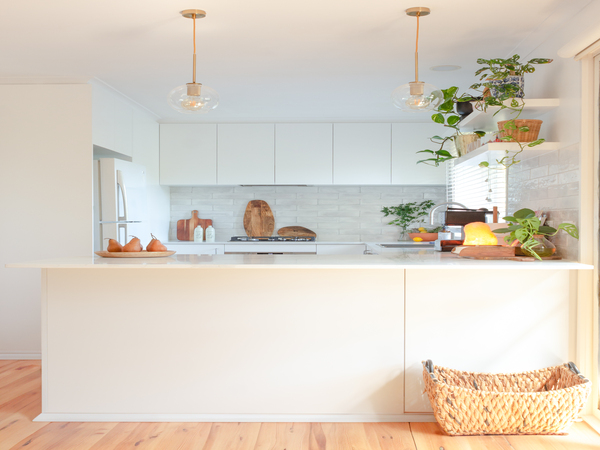 Bright kitchen with white cabinets, hanging lights, plants, and a wicker basket on a wooden floor.