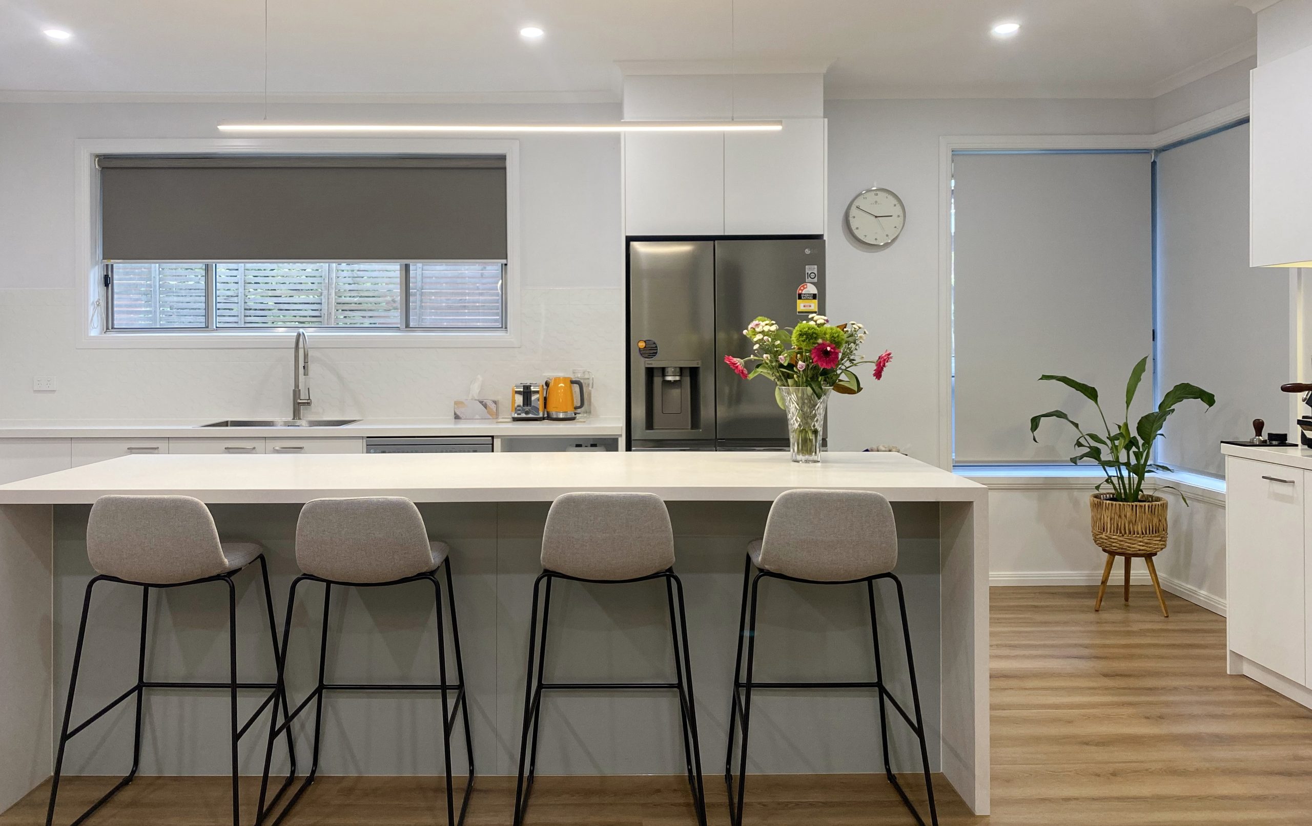 , four stools, stainless steel appliances, flowers on counter, and wooden floor. Modern kitchen with island, four stools, stainless steel appliances, flowers on counter, and wooden floor.