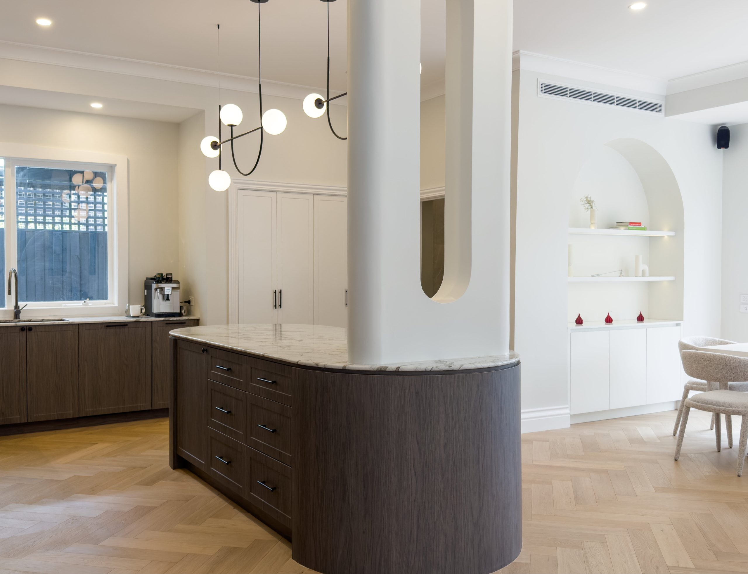 Curved dark timber island bench with marble benchtop, herringbone floors and arched joinery Curved dark timber island bench with marble benchtop, herringbone floors and arched joinery