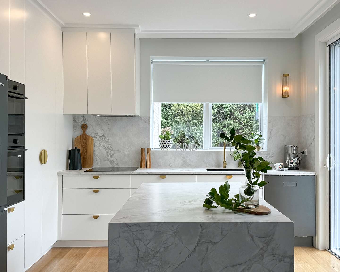 White kitchen with marble waterfall island, brass handles and matching stone splashback