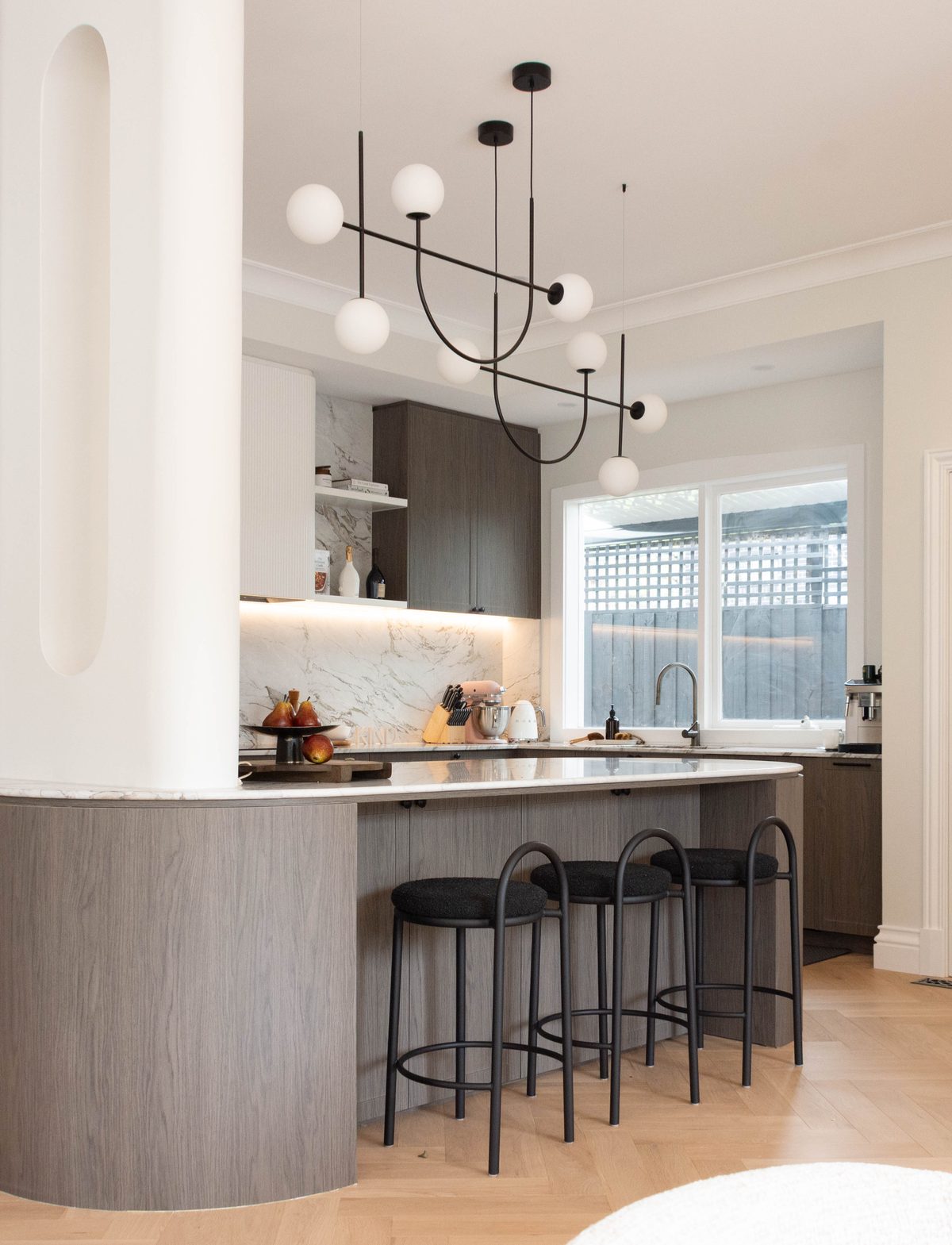 A KIND kitchen with curved joinery, stone benchtop and counter stools
