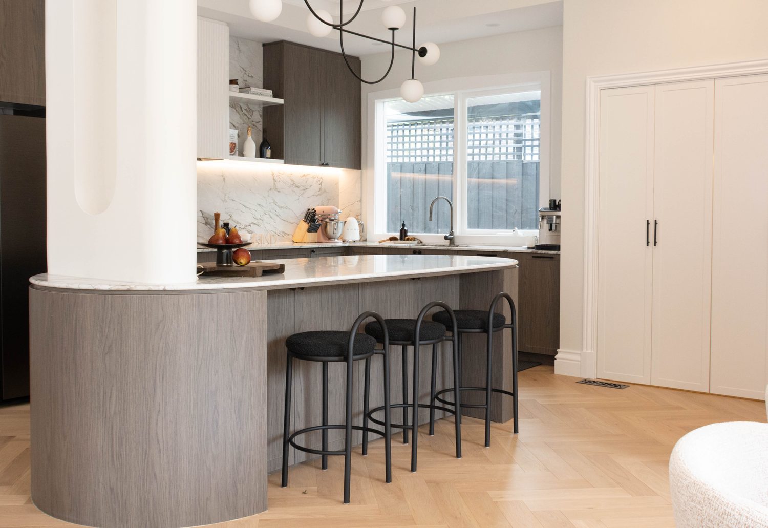 A KIND kitchen and dining space with herringbone flooring and curved island